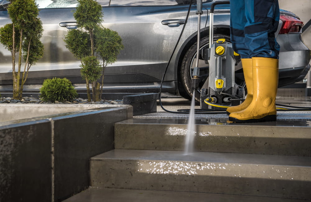 Modern Homeowner Washing His Garden Paths and Driveway Using Powerful Pressure Washer Next to His Car