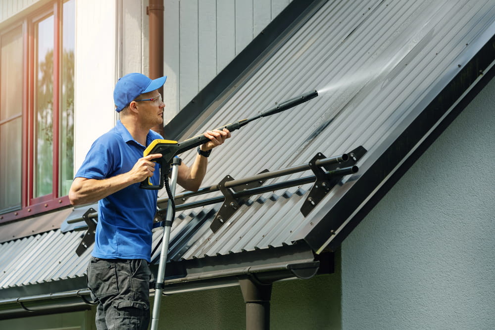 Man standing on ladder and cleaning house metal roof